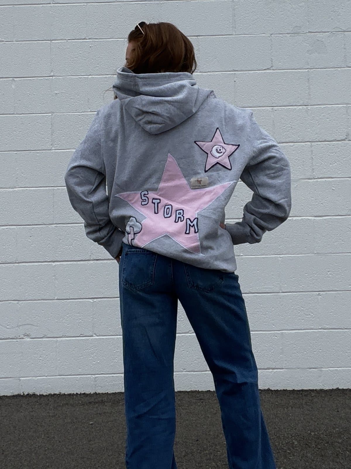 The back of a grey hoodie with a pink patchwork star and STORM lettering
